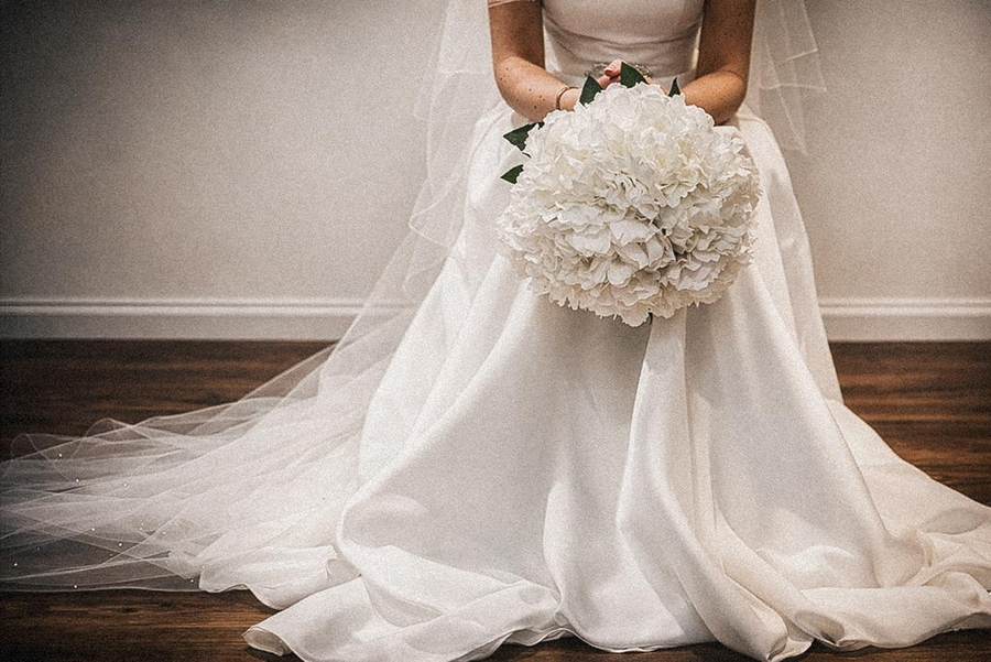 Bride seated with her white hydrangea bouquet in her lap