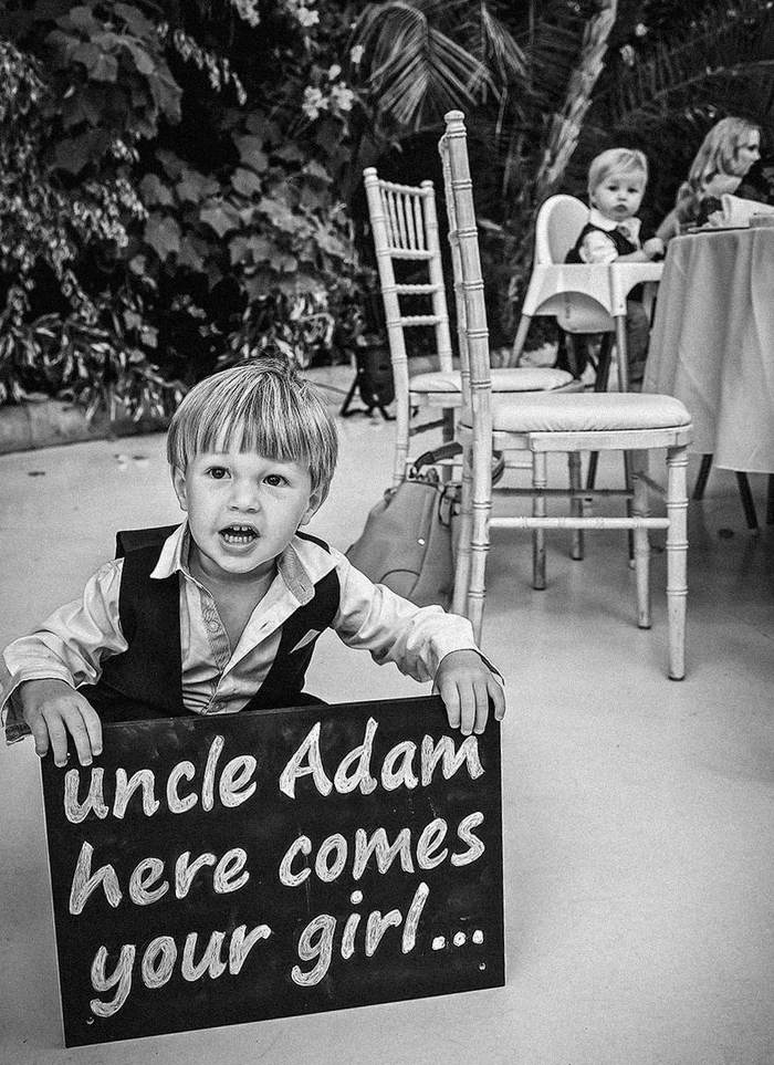 A page boy holding a chalkboard sign announcing the bride