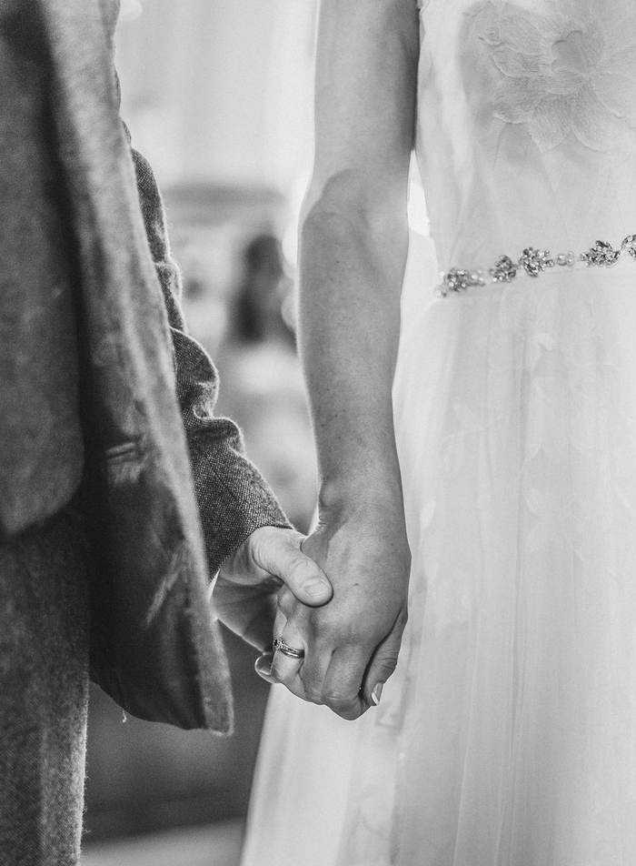Black and white detail of a couple holding hands at the altar