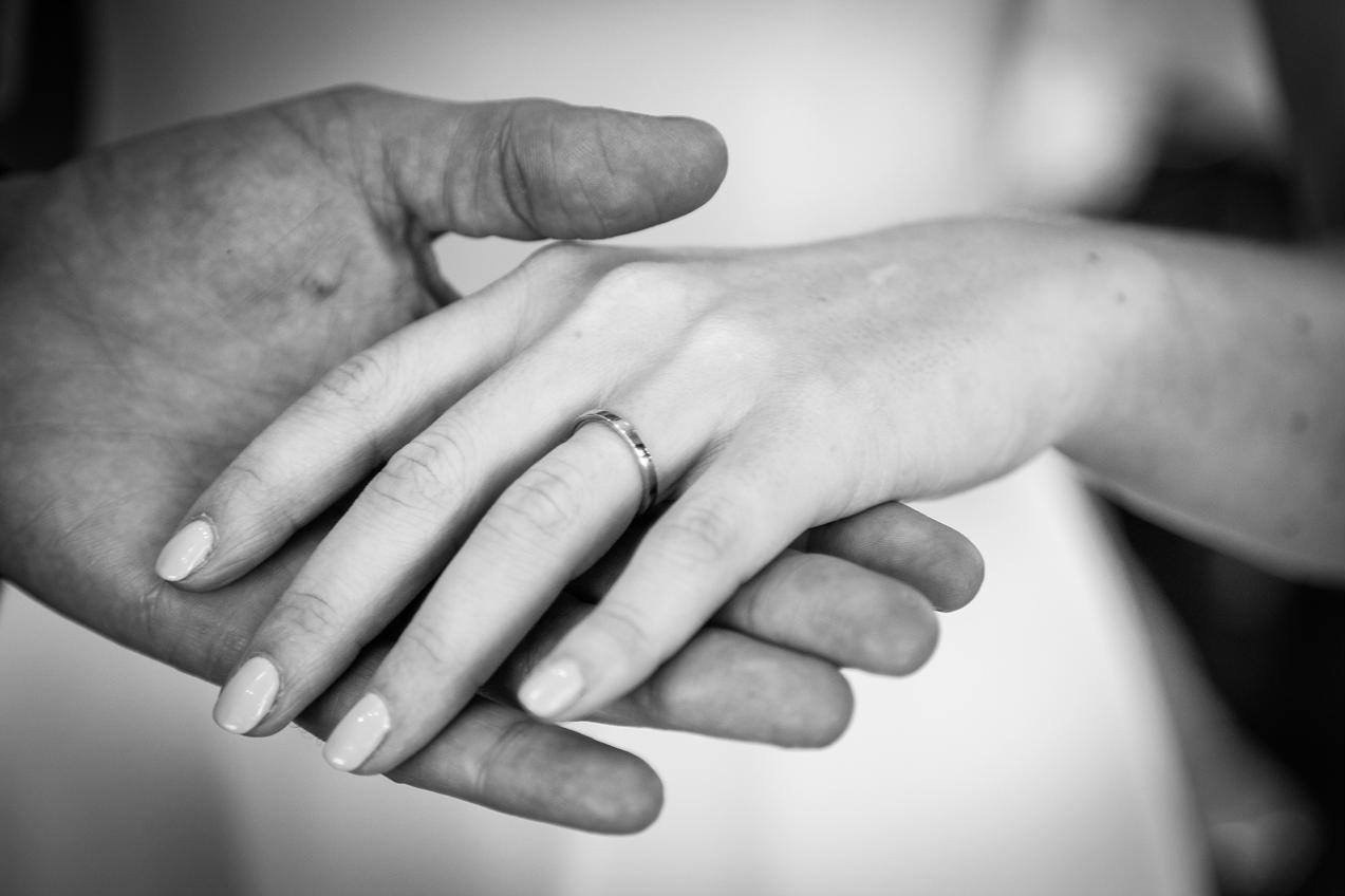 Black and white close-up of a new wedding ring on a bride's hand resting in her husband's