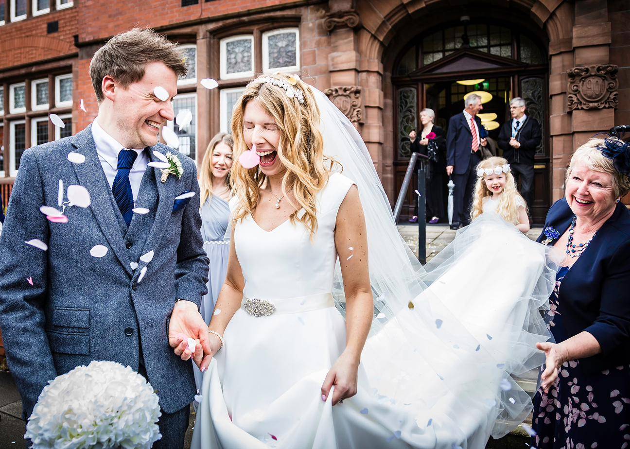 Newlyweds laughing as guests throw confetti on the steps outside the church