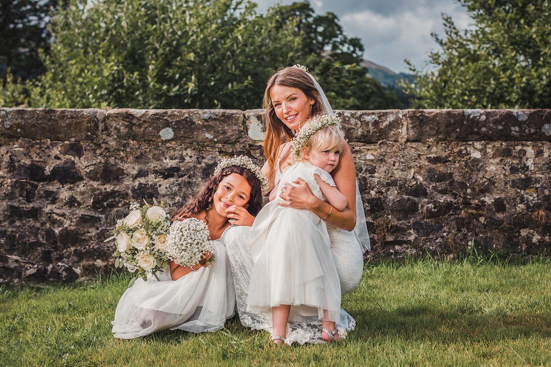 A bride sitting on the grass with two young flower girls