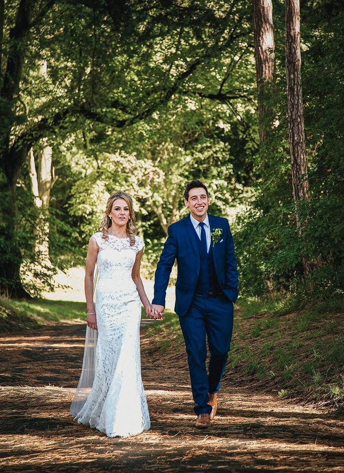 Bride and groom walking hand in hand along a sunlit woodland path