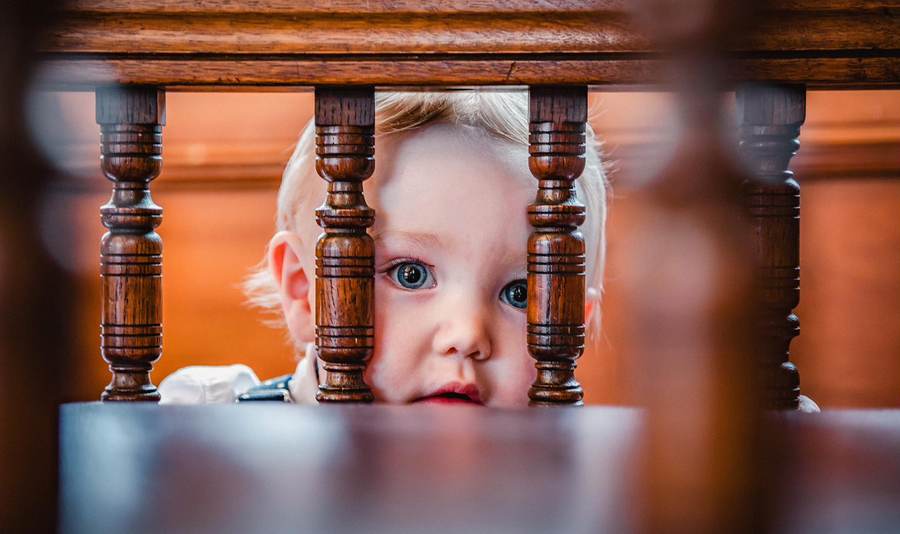 A small child peeking through the wooden rails of a church pew