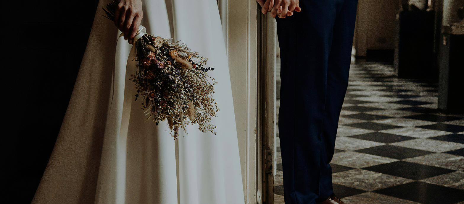 A bride holding a dried-flower bouquet beside her groom on a black and white chequered floor