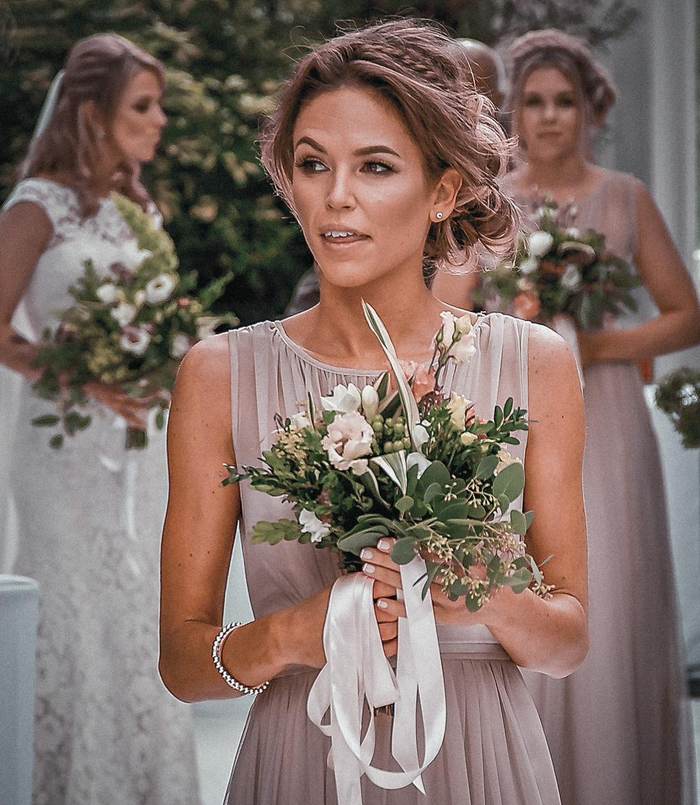 A bridesmaid in blush pink holding a bouquet tied with ribbon