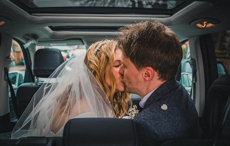 Newlyweds kissing in the back of the wedding car